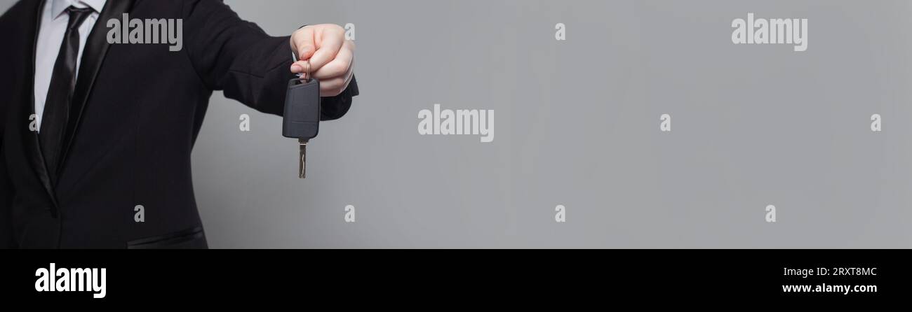 Young adult businessman in a suit giving a car keys on grey background, closeup Stock Photo