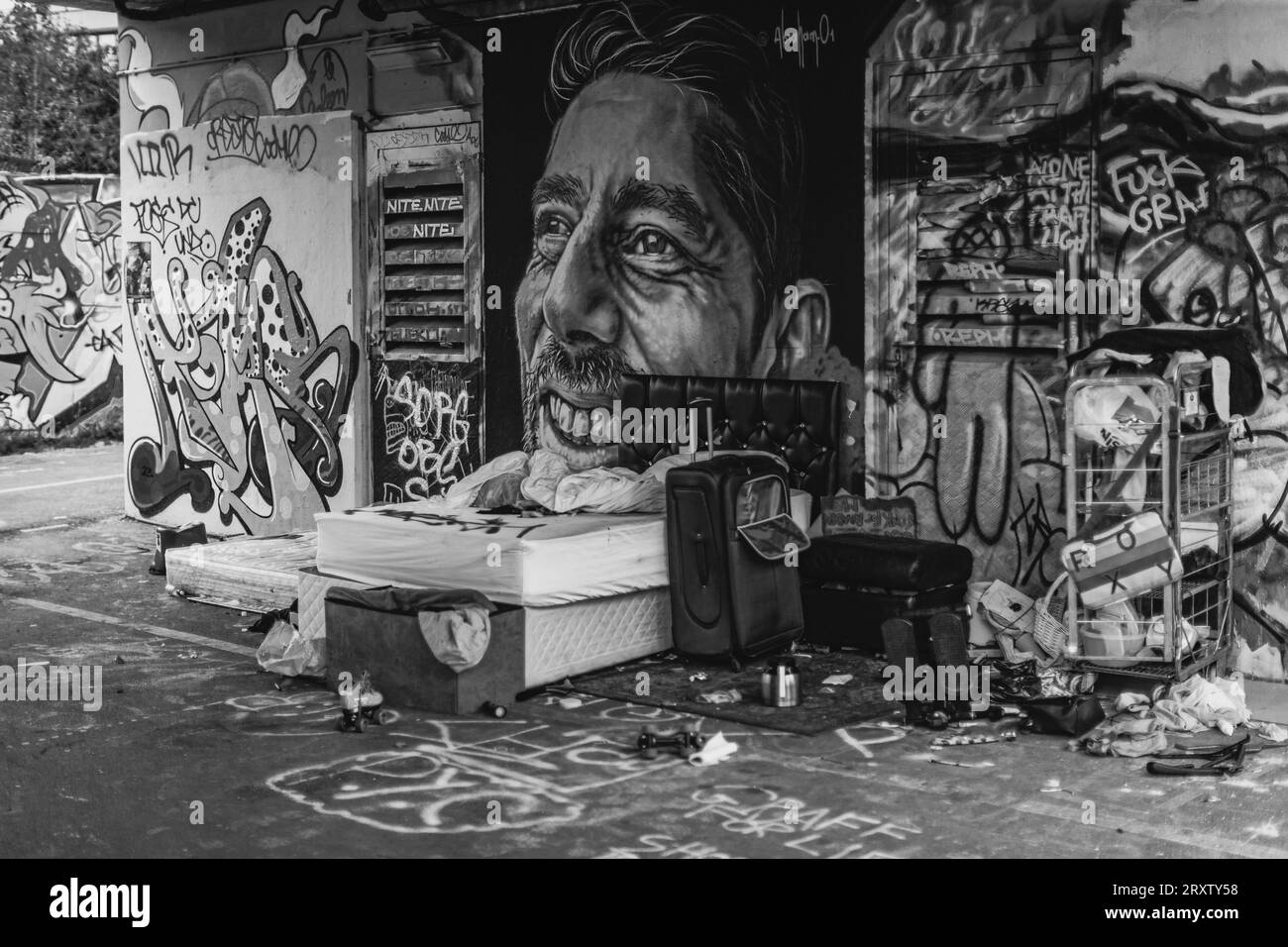 Black and white street scene of an abandoned bed under a bridge in east