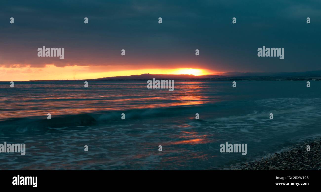 Dramatic sunset in the coast. Orange dramatic colours on cloudy sky. End of day. Sun on the horizon. Stock Photo