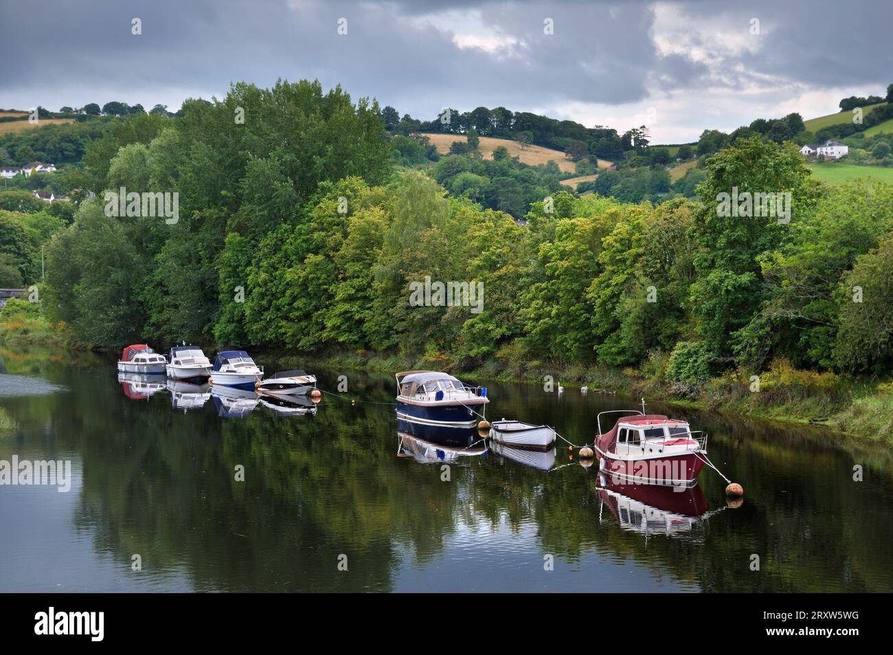 Line of boats moored on the River Dart with trees and rolling hills landscape on a cloudy day in summer. Totnes, South Hams, South Devon, England, UK Stock Photo