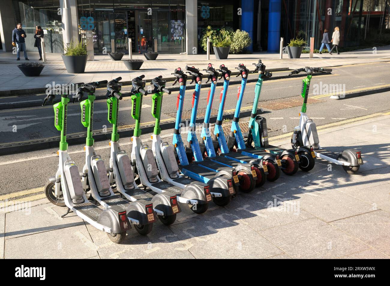 A line of electric scooters from Lime, Dott and Tier for hire / rental parked on a pavement in