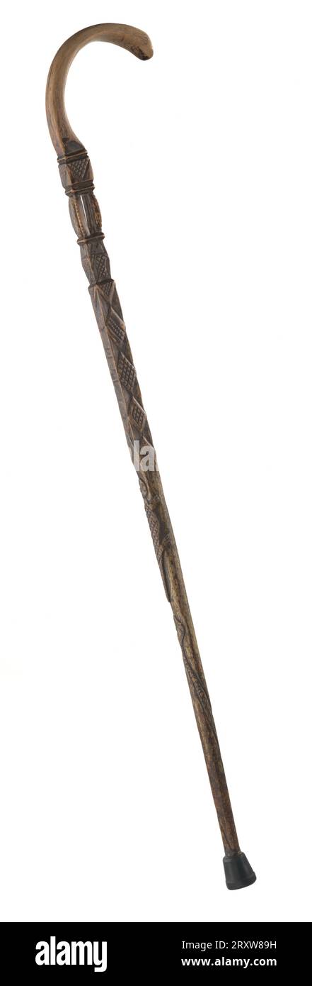 A carved wooden walking cane owned by Sen. W.B. Nash. The main section of the cane is round at the bottom but squared off about halfway up. The cane has been incised over much of its surface with geometric and animal decorations, including diamonds, fish, snake and lizard. 1911 is carved on the outward facing side of the cane. Near the head of the cane is a carved chamber with four curved posts inside which rolls a loose wooden ball. The top of the cane is curved, pale and very smooth from use. At the tip of the cane handle is another incised section, a geometric design or possibly letters. Th Stock Photo