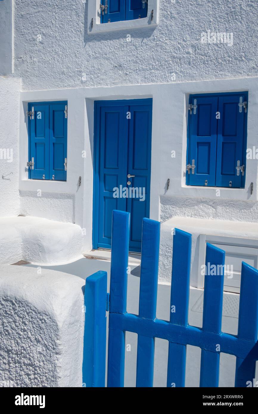 Traditionally painted Santorini house of blue and white - foreground blue wooden gate and building of whitewashed stone and blue wooden window shutter Stock Photo