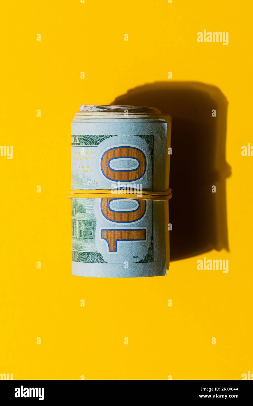 Wad of 100 USD dollar banknote bills on a yellow background, Roll of American dollar banknote bills on a yellow background Stock Photo
