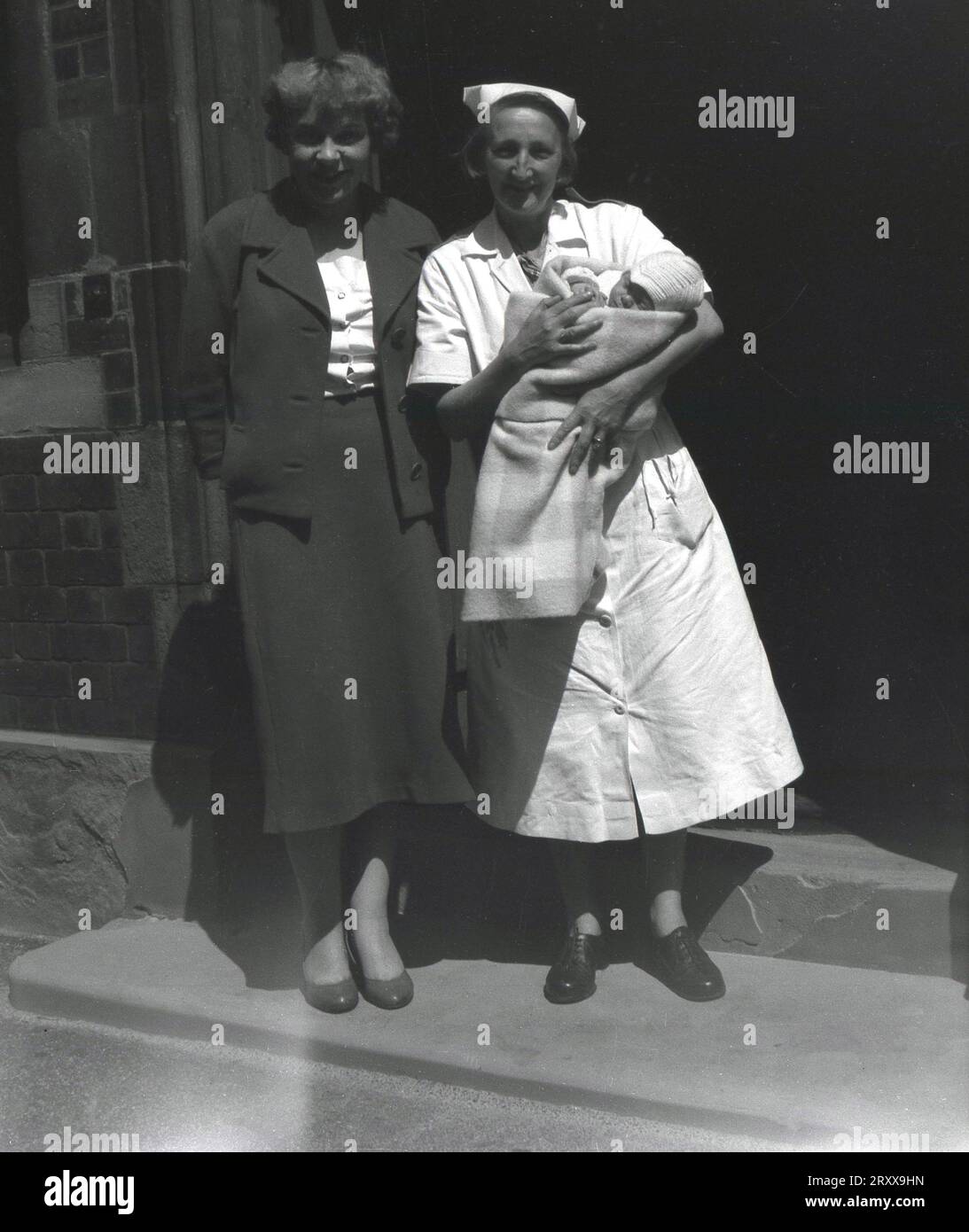 1960s, historical, summertime and at the entrance to a stone built buidling, a nurse holding a new baby, standing outside for a photo with its new mother, Manchester, England, UK. Stock Photo
