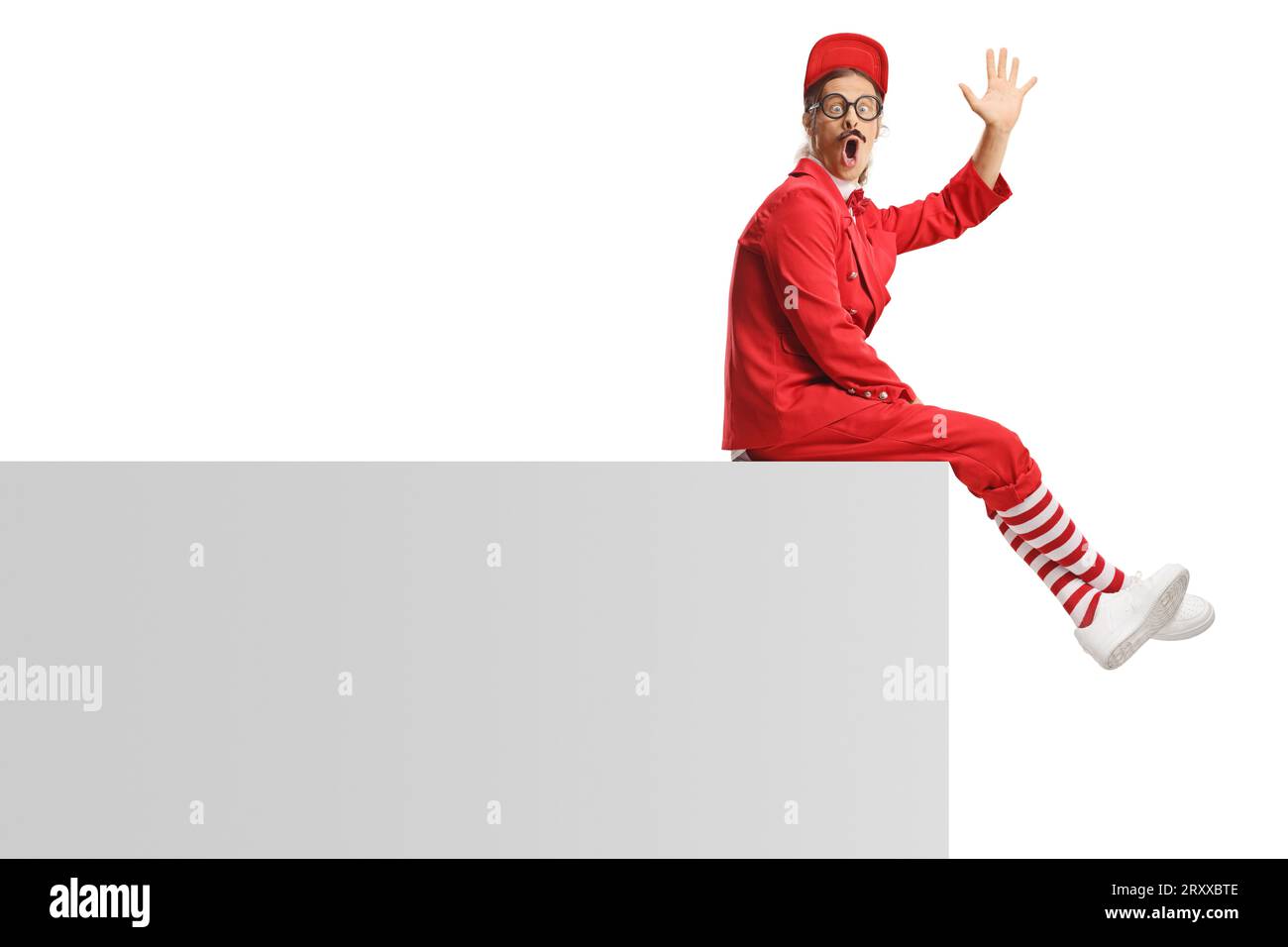 Funny entertainer in a red suit sitting on a wall and waving isolated on white background Stock Photo