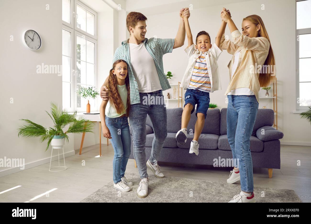 Happy family are playing together, boy is jumping from sofa holding hands parents in living room. Stock Photo