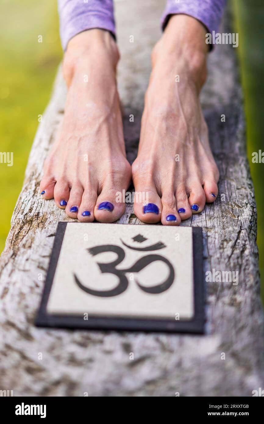 Close up of woman's feet behind an Om sign on a tree trunk over the water Stock Photo