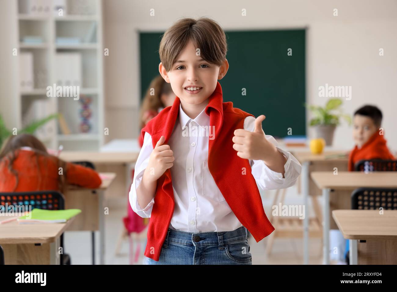 Little schoolboy showing thumb-up in classroom Stock Photo - Alamy