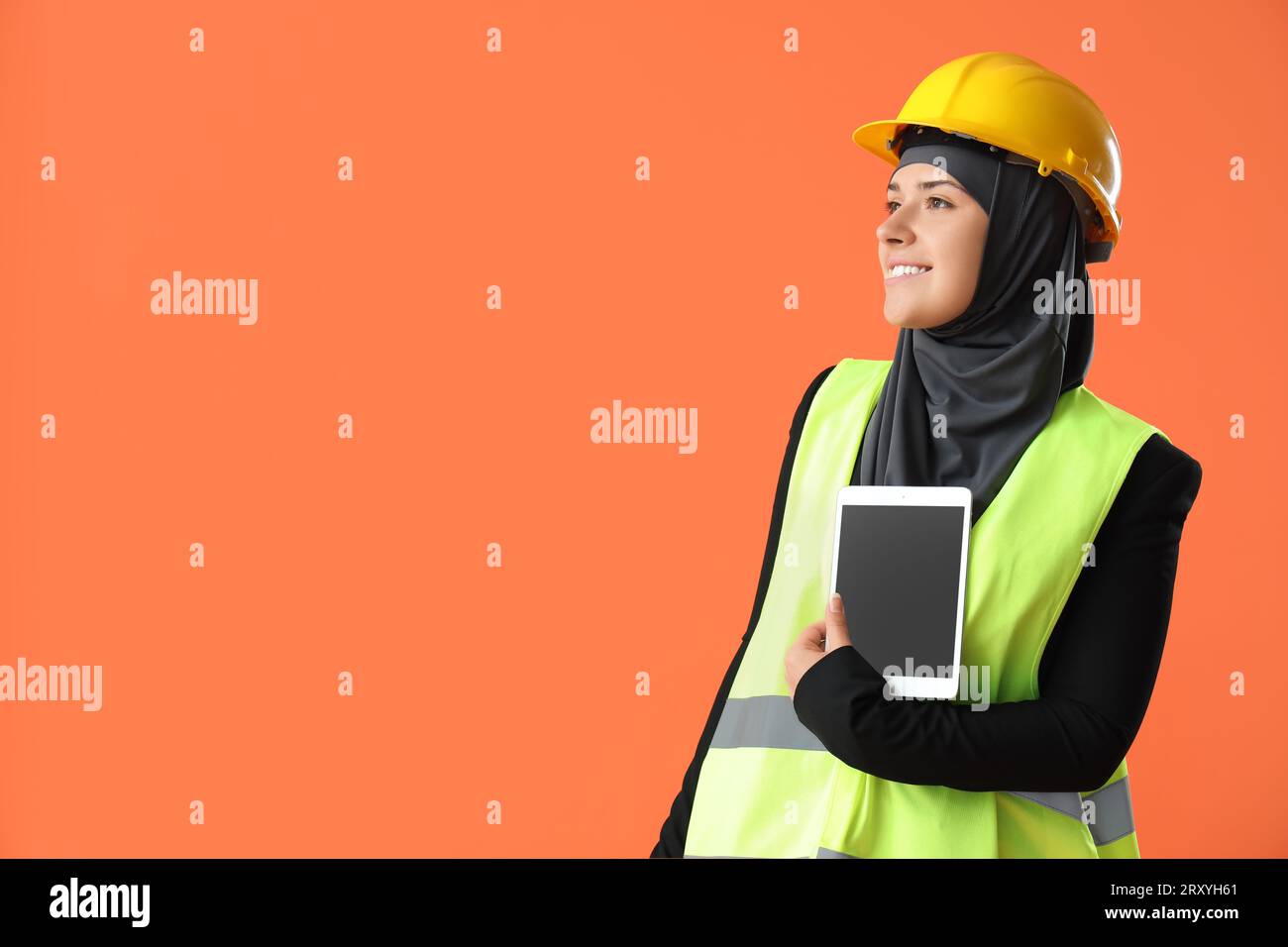 Female Muslim construction worker with tablet computer on orange background Stock Photo