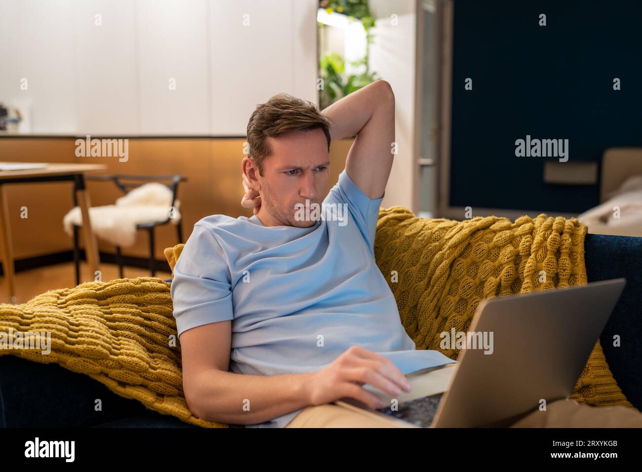 Tired serious man working on laptop at home lying on couch, overworking, workaholic. Stock Photo