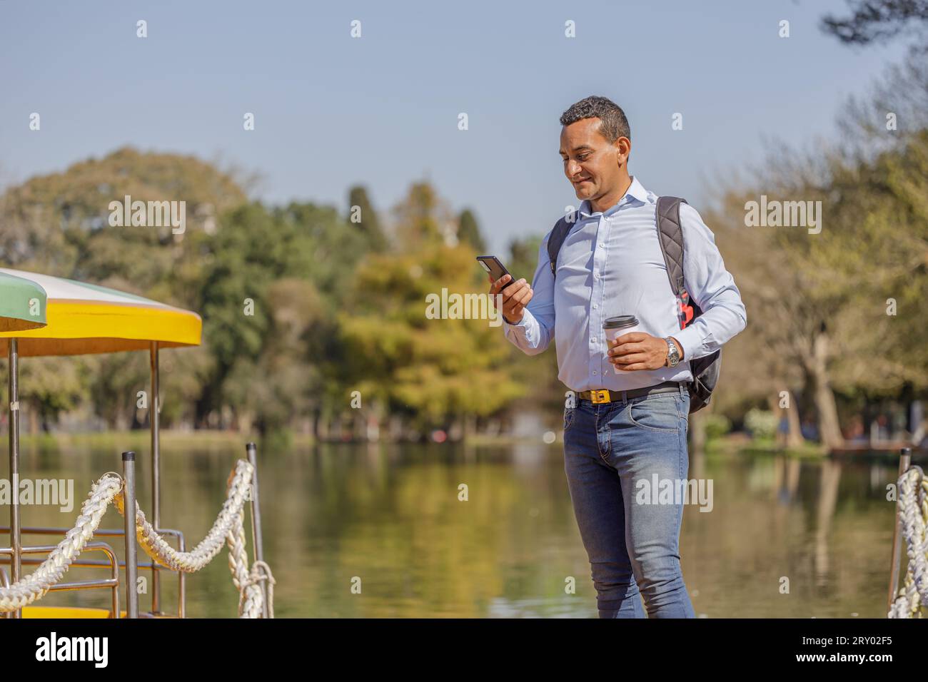Latin man using a mobile phone on a dock on the shore of a lake. Stock Photo