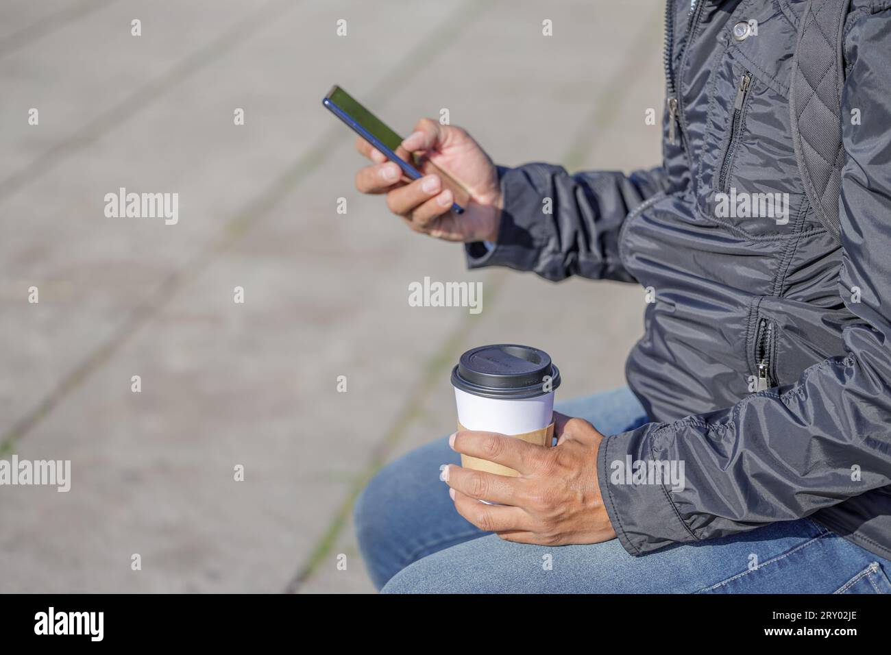 Detail of the hands of a Latin man holding a disposable cup with coffee and a mobile phone. Stock Photo