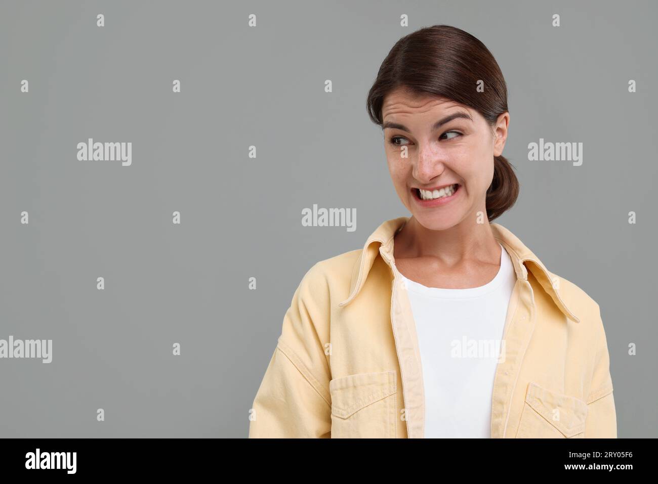 Portrait of embarrassed young woman on grey background, space for text ...