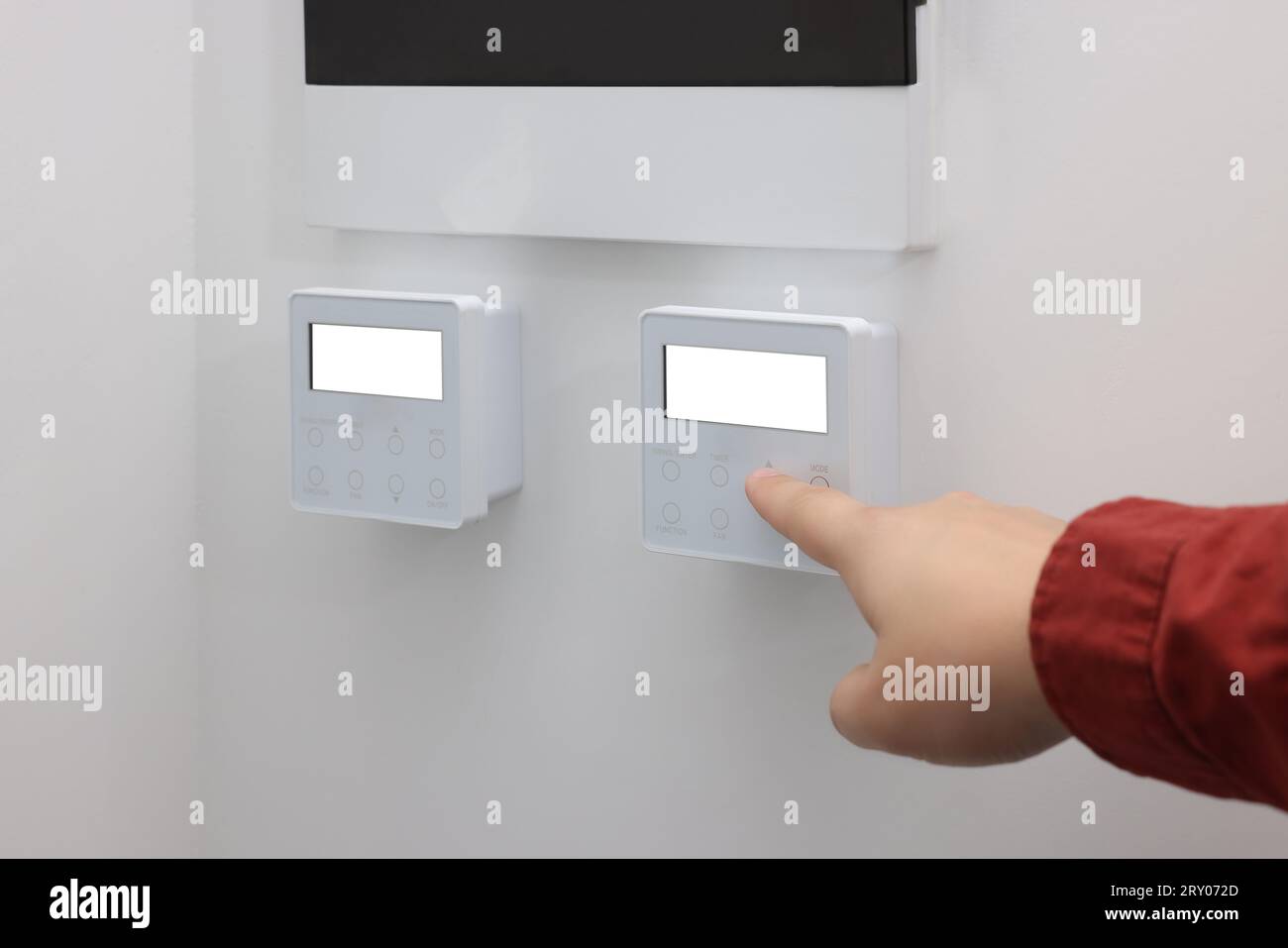 Man adjusting thermostat on white wall, closeup. Smart home system Stock Photo