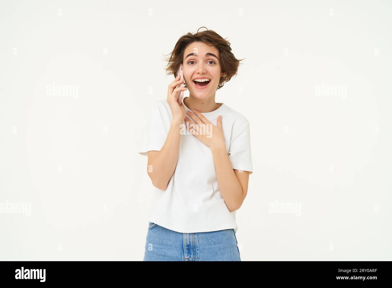 Portrait of chatty young woman talking on mobile phone, laughing and smiling, answer telephone with surprised face, standing over white background Stock Photo