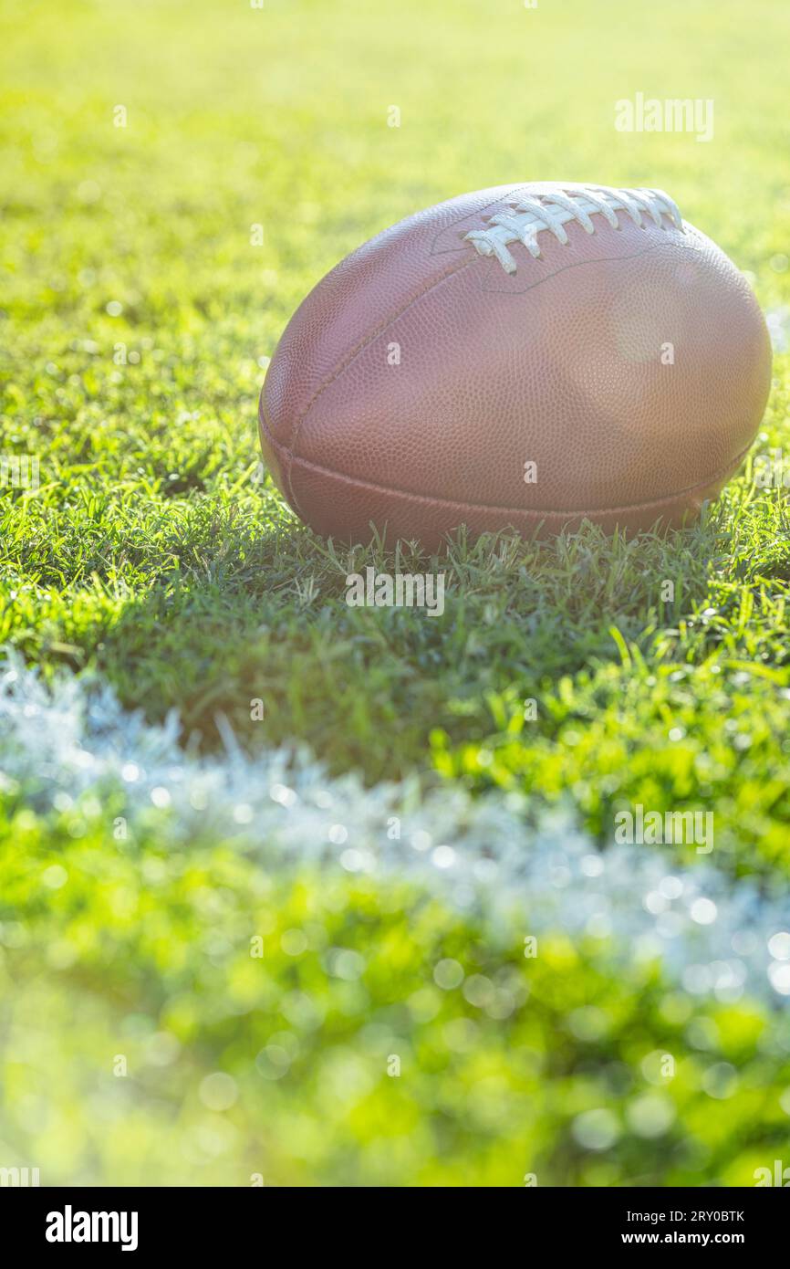 A low angle close-up view of a leather American Football sitting in the grass next to a white yard line with hash marks in the background, lens flare. Stock Photo