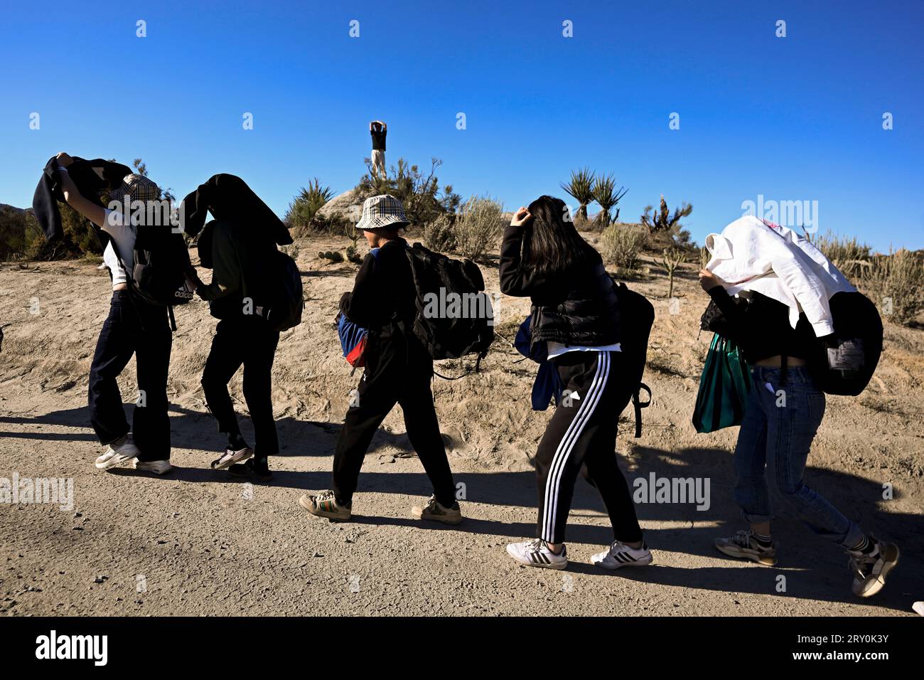 Three migrants who had managed to evade National Guard and cross the Rio  Grande onto U.S. territory wait for Border Patrol along a wall set back  from the geographical border, in El