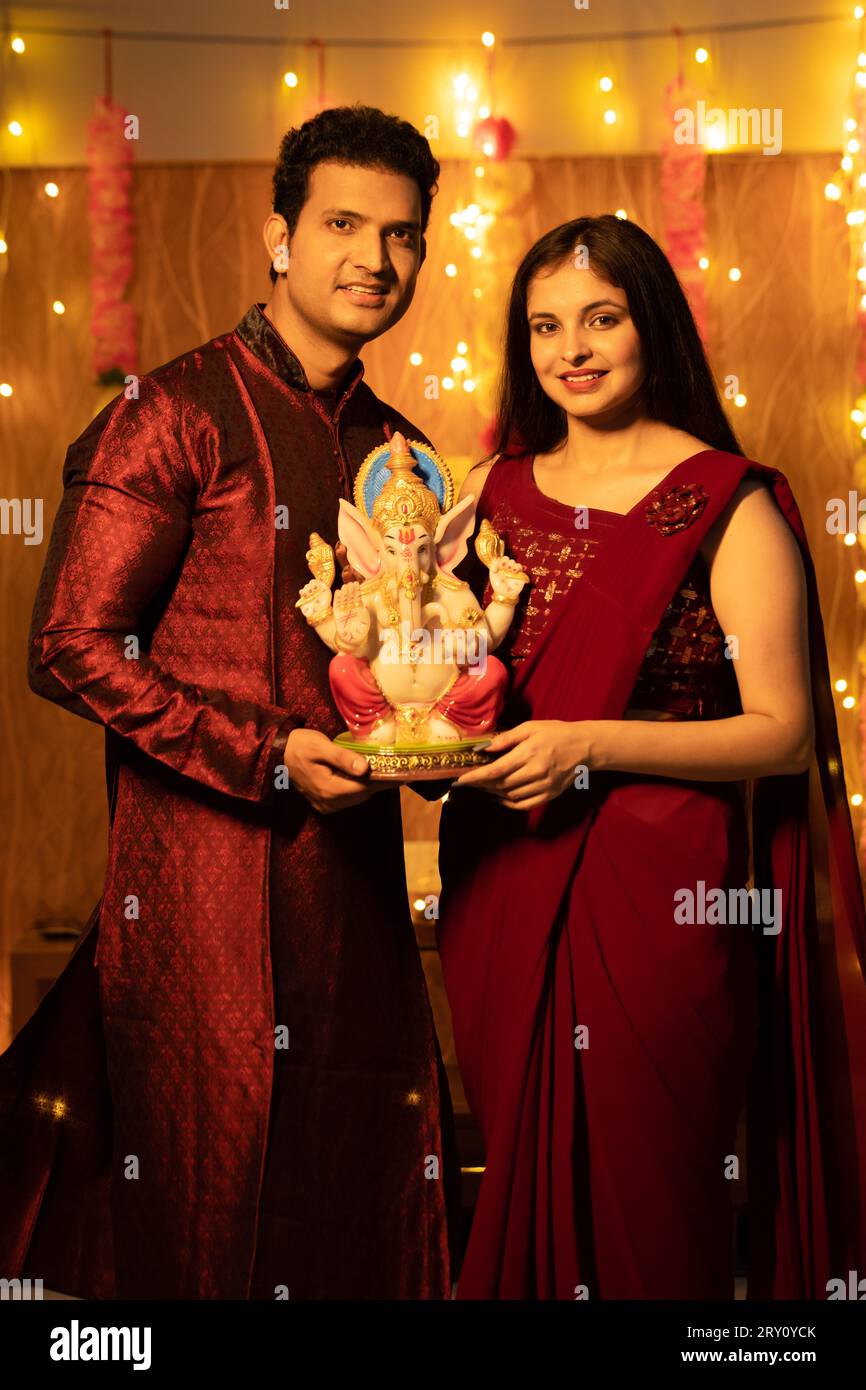 Happy young Indian couple in traditional dress holding Ganesh idol or ...
