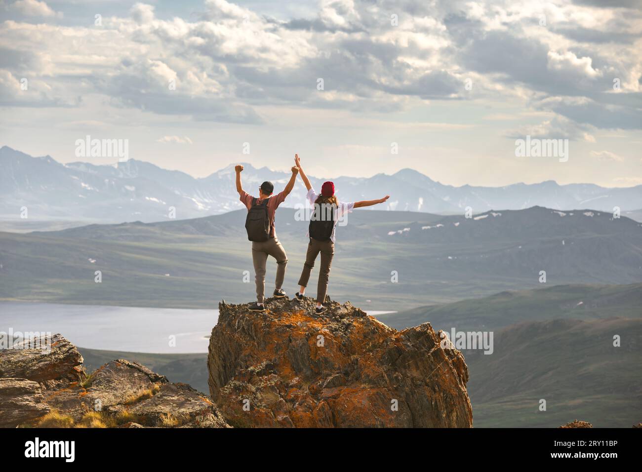 Young couple of hikers with backpacks are standing at mountain top with open arms in winner pose Stock Photo