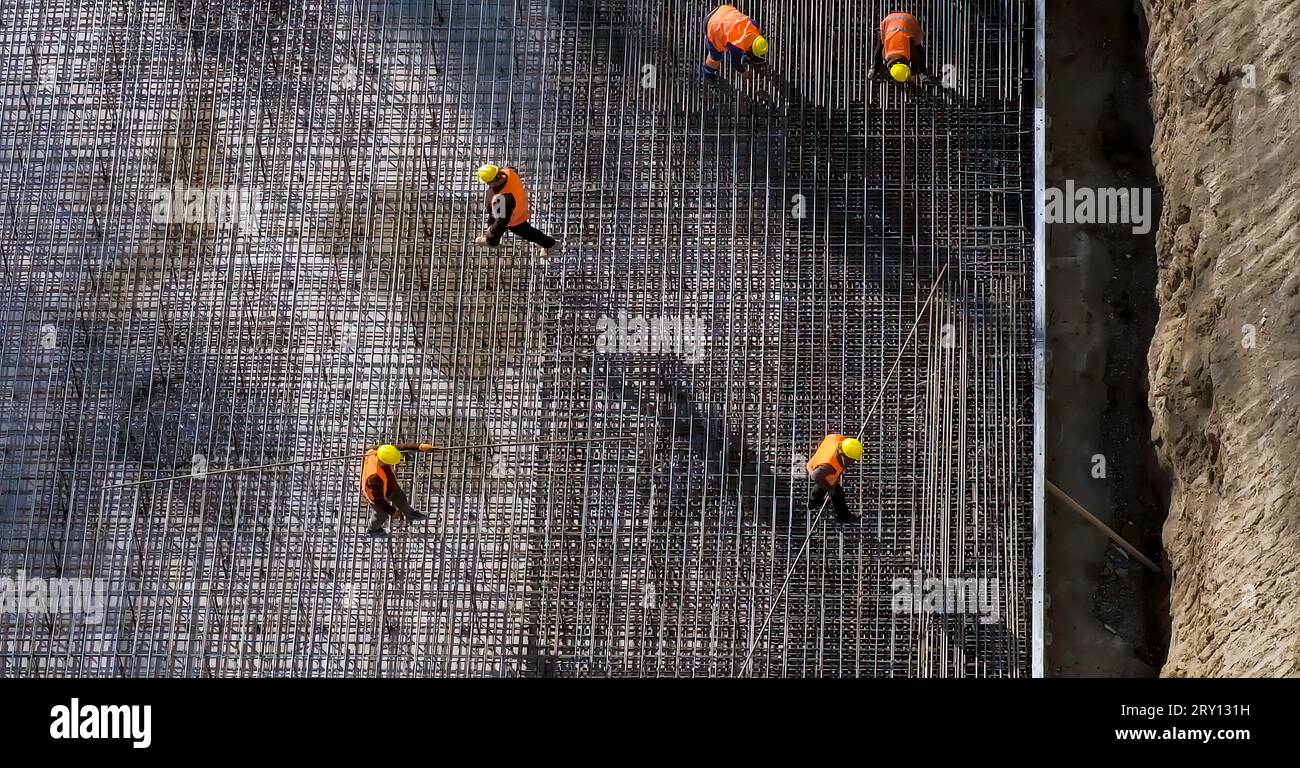 Construction site. Workers in orange uniform carrying steel bars