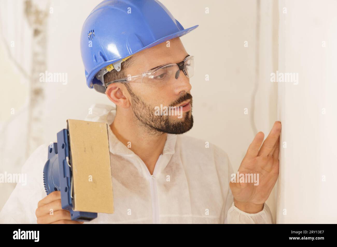 builder in hardhat sanding wall indoors Stock Photo