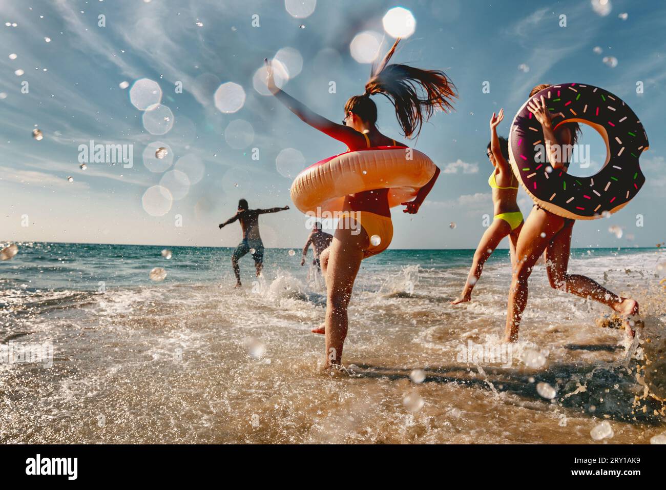 Old style photo of group of friends are having fun and running to sea beach with inflatable donuts Stock Photo