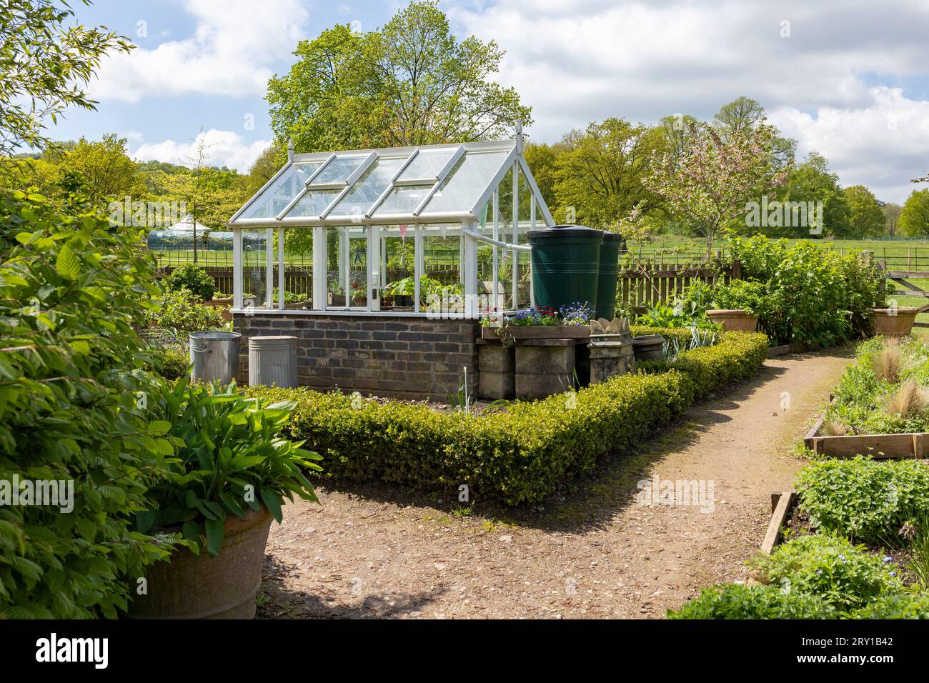 A garden plot with seedbeds and a glass greenhouse in the centre of