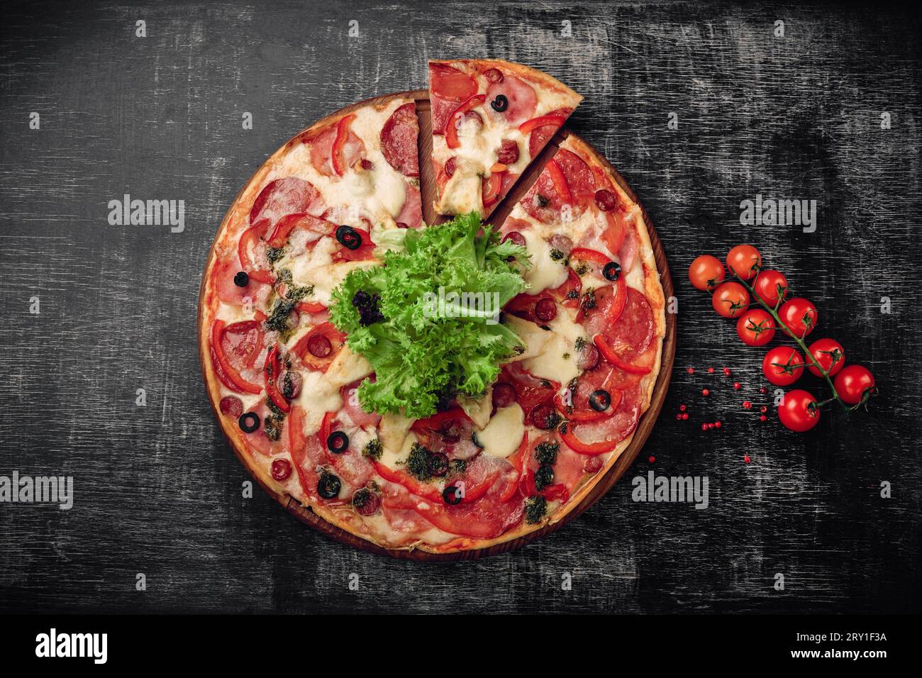 Pizza with ham, salami, cheese, mushrooms, cherry tomatoes, bell peppers and salad on a black chalk board, top view. Stock Photo