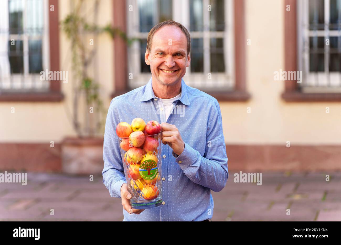 28 September 2023, Hesse, Frankfurt/Main: Martin Heil, chairman of the Association of Hessian Cider and Fruit Juice Presses (Verband der Hessischen Apfelwein- und Fruchtsaft-Keltereien e.V.), holds an oversized cider glass (Geripptes) with apples from meadow orchards and the demand 'Save the orchards', while the Association of Hessian Cider and Fruit Juice Presses (Verband der Hessischen Apfelwein- und Fruchtsaft-Keltereien e.V.) informs about the start of the pressing season, the apple harvest and trends and expectations for this year's cider. Photo: Andreas Arnold/dpa Stock Photo