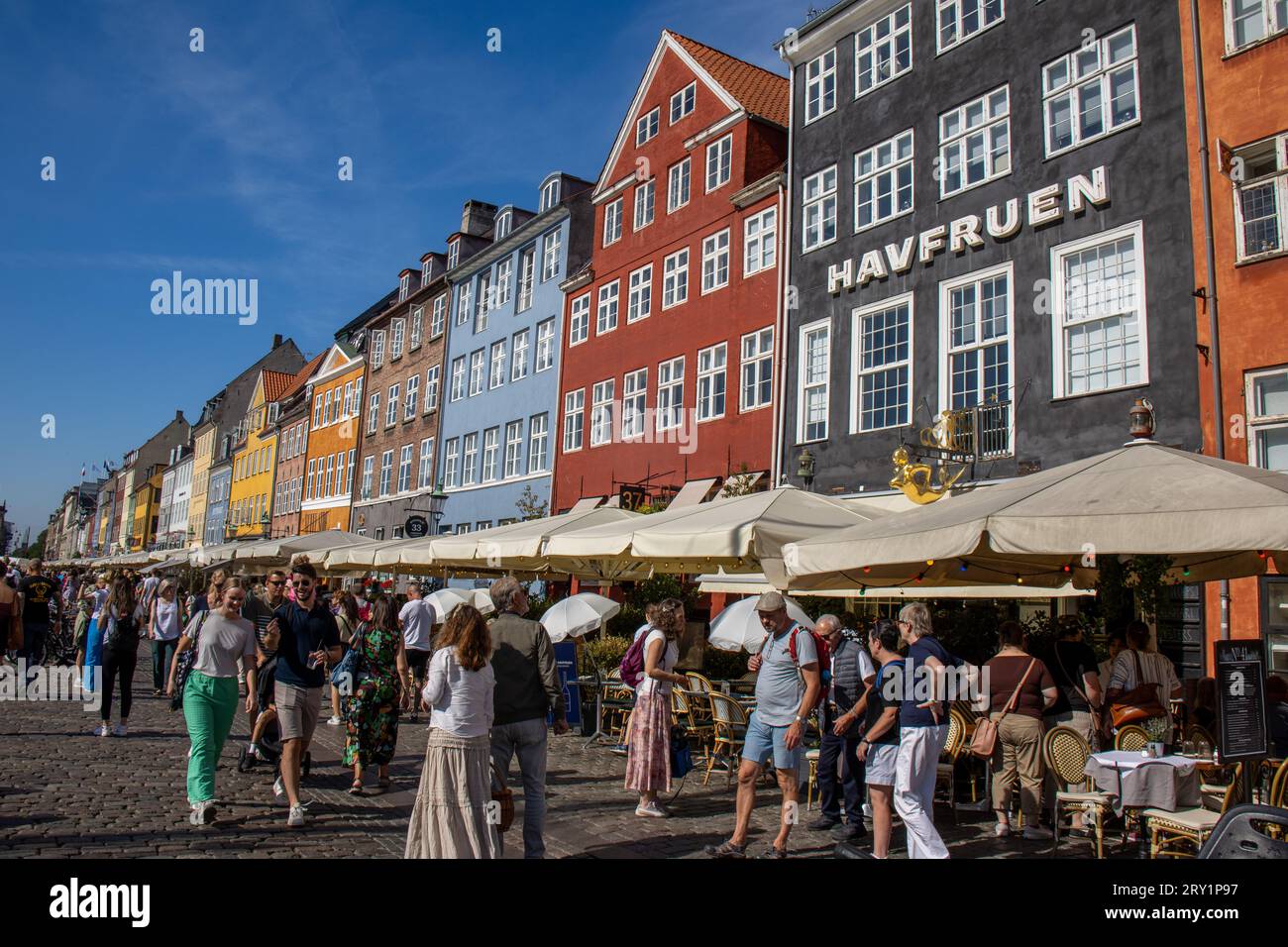 Gente llenando el paseo marítimo y las terrazas junto al canal en Nyhavn, uno de los lugares con más encanto de Copenhague con sus casas coloridas. Stock Photo