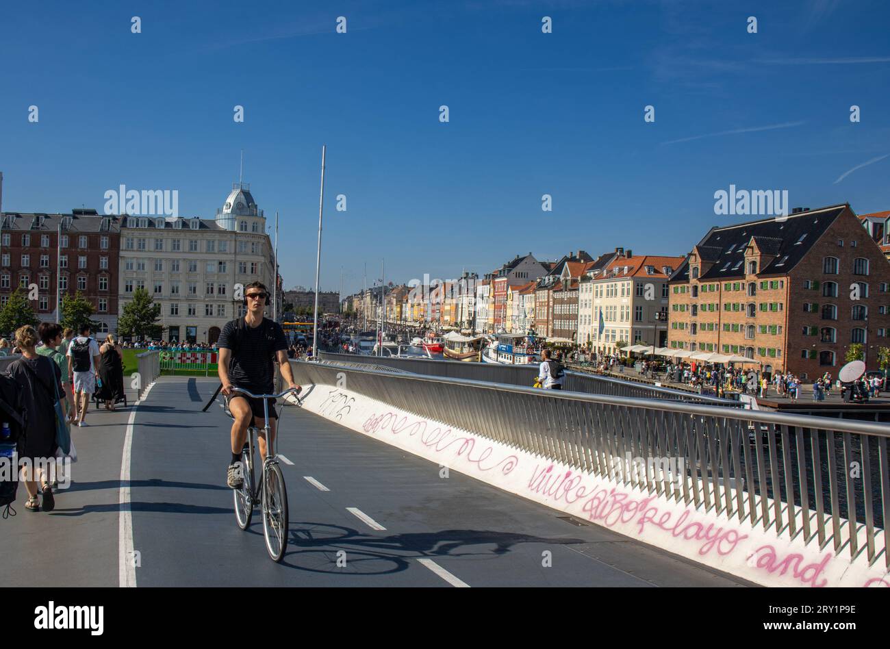Uno de los miles de ciclistas que cada día recorren las calles y puentes de Copenhague. Al fondo, las coloridas casas y barcos de Nyhavn. Stock Photo