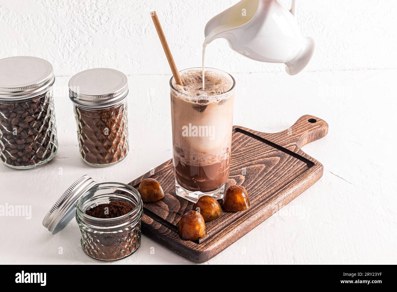 A stream of milk from a jug is poured into a tall glass of icecold