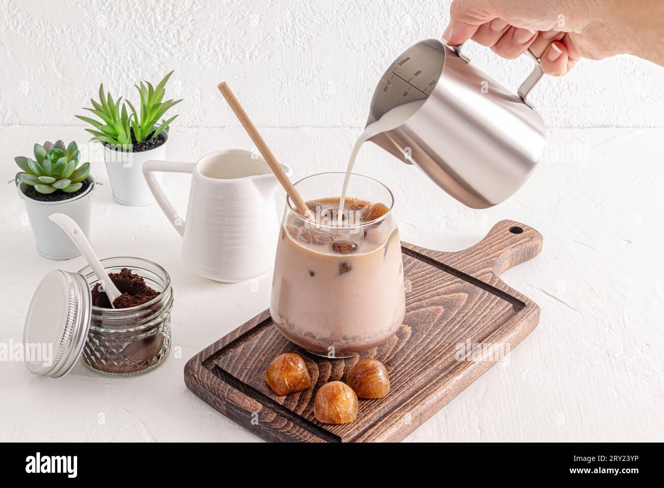 A stream of milk from a metal jug is poured into a large glass of ice
