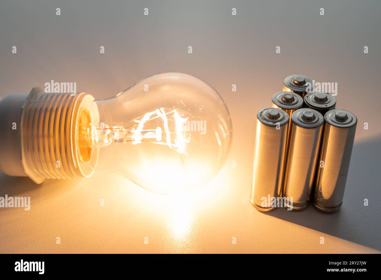 Light bulb turned on, with batteries next to it. Accumulation and reuse
