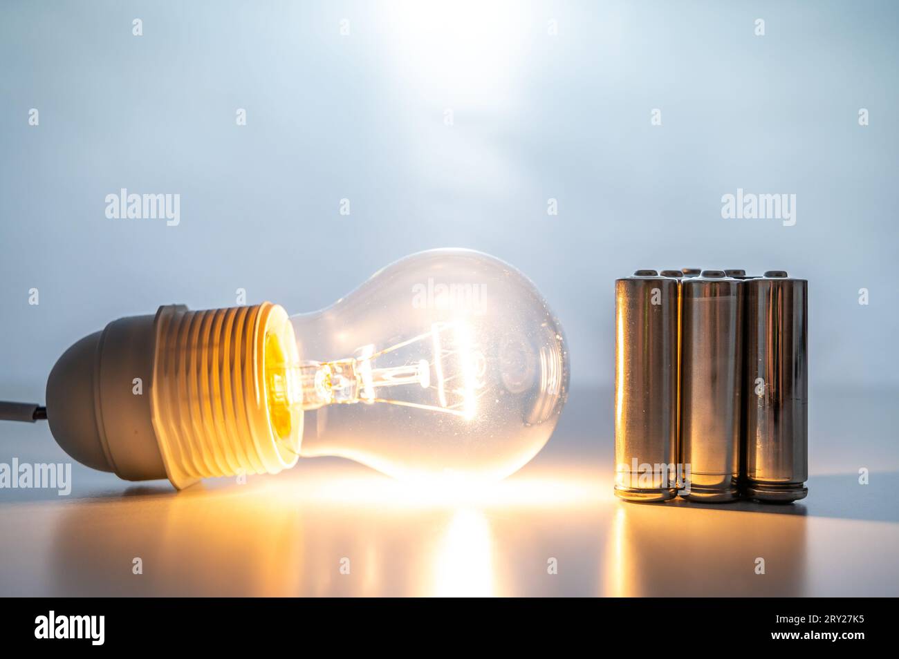 Light bulb turned on, with batteries next to it. Accumulation and reuse