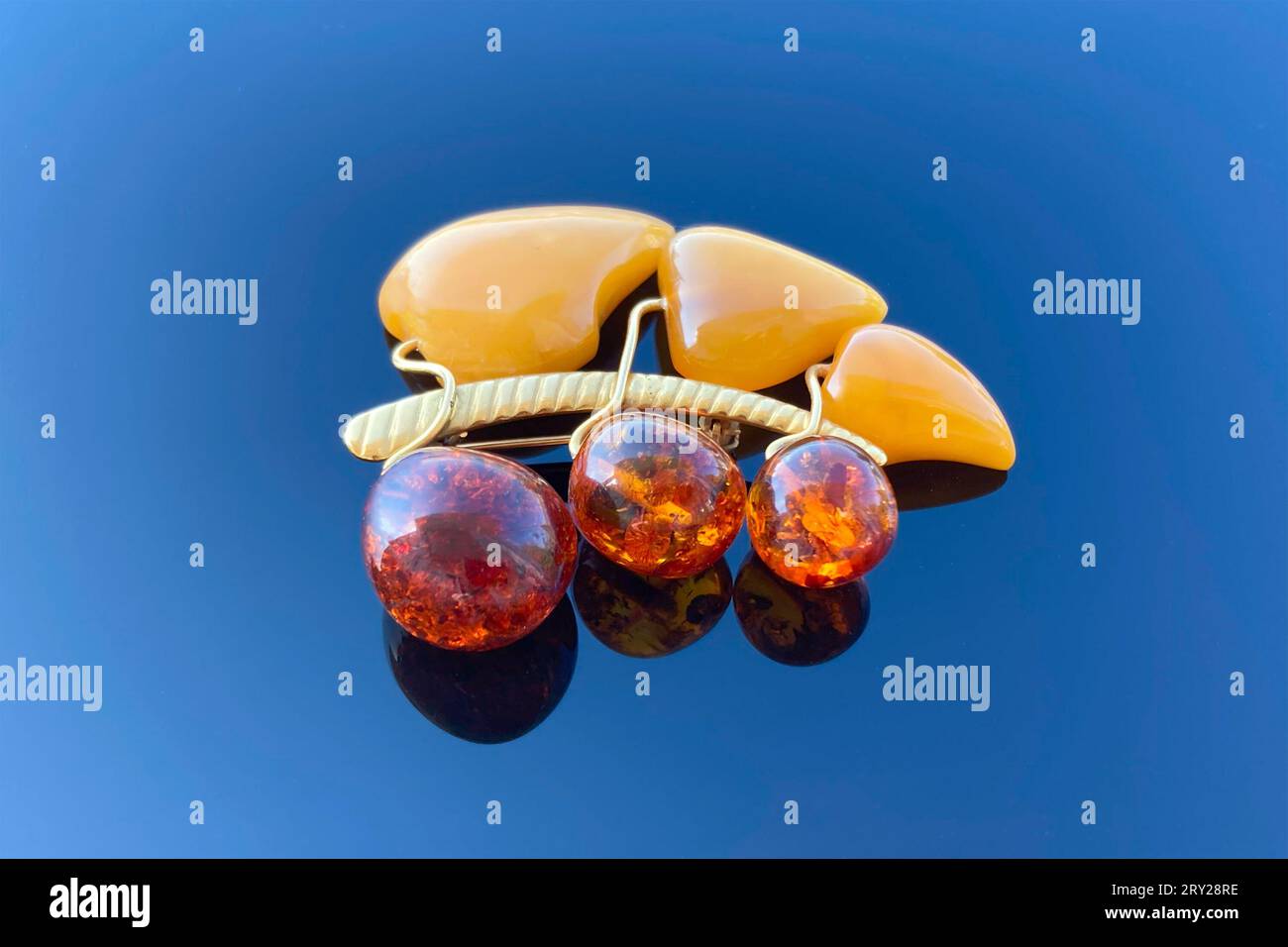 vintage brooch berries and leaves with of amber and brass, made in USSR on blue glossy background Stock Photo