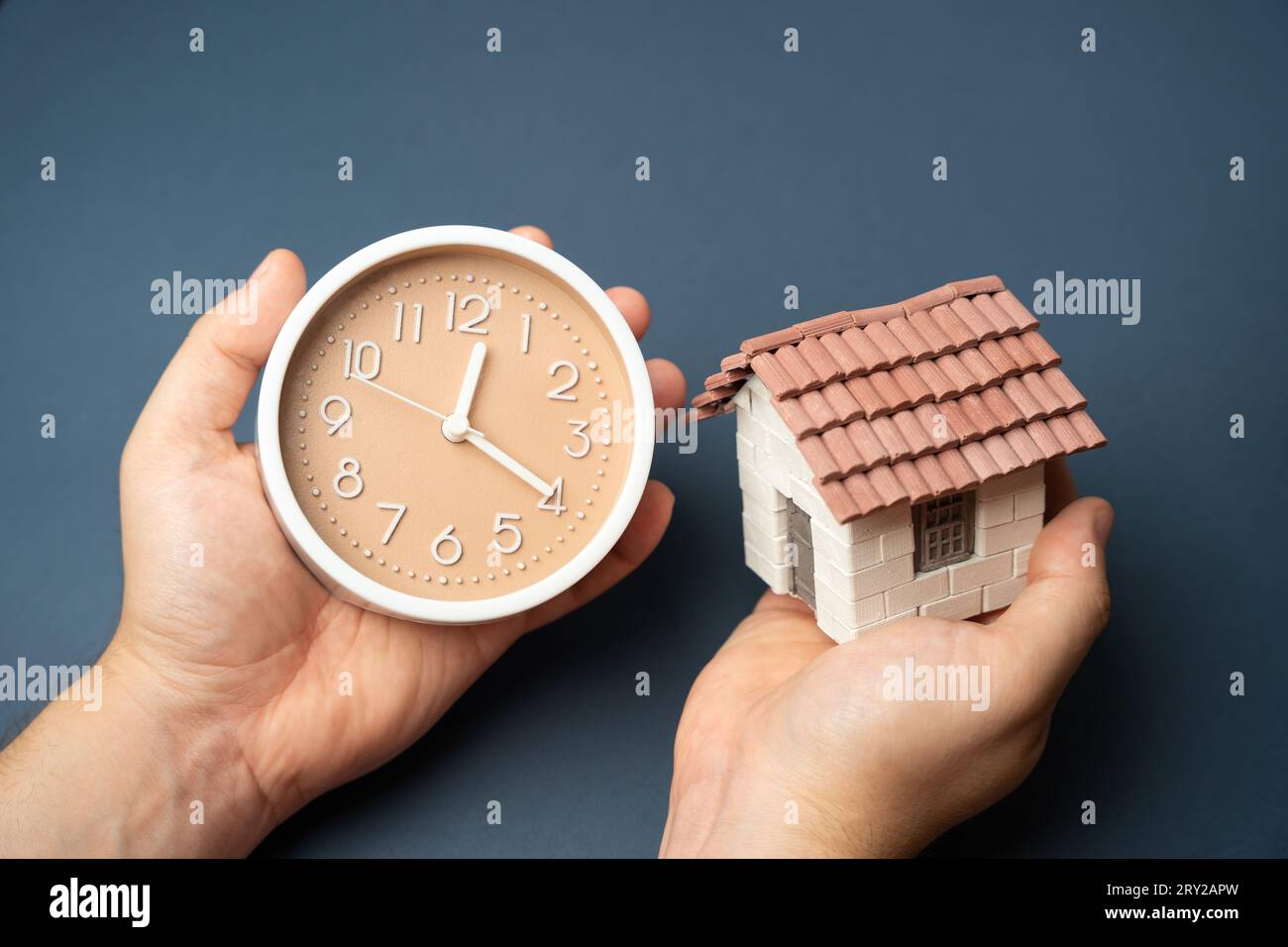 House and clock in hands. Importance of cherishing every moment spent with loved ones. Allocate time for relaxation and self-care amidst busy schedule Stock Photo