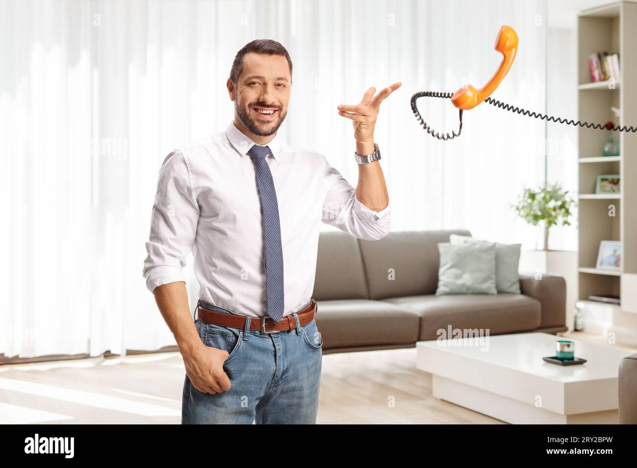 Cheerful man throwing a rotary phone handset in a living room Stock