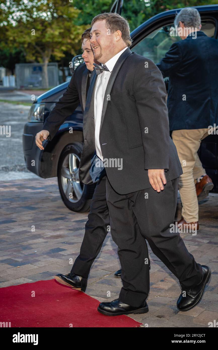 Two young men with Down syndrome walk with confidence and joy towards the red carpet from their car, embodying the spirit of inclusivity Stock Photo