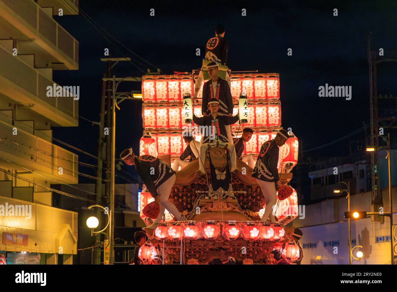 Kishiwada, Japan - September 17, 2023: Young men with lanterns and traditional clothing atop portable shrine at night festival Stock Photo