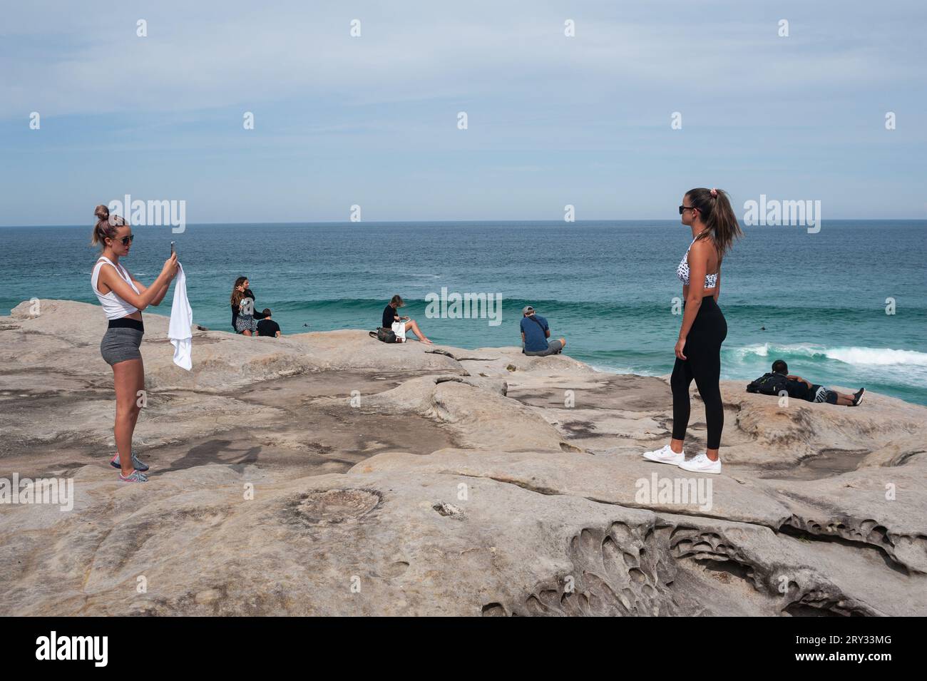 27.09.2019, Sydney, New South Wales, Australia - Young woman photographs her friend on the cliffs at Tamarama Point along Bondi to Bronte Coastal Walk. Stock Photo