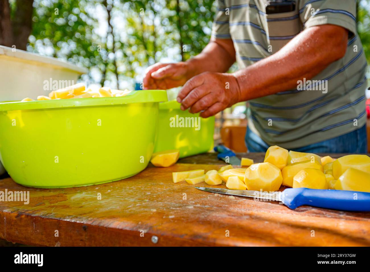 https://c8.alamy.com/comp/2RY37GW/an-elderly-farmer-cooker-cuts-potatoes-using-knife-into-slices-on-the-wooden-board-prepares-it-for-cooking-at-the-outdoor-bowls-are-full-of-cut-vege-2RY37GW.jpg