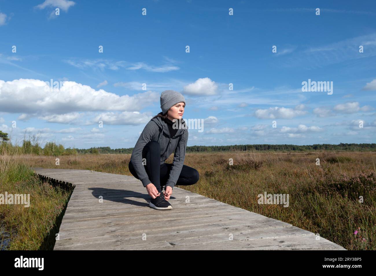 Fitness woman runner tying shoelace on wetland boardwalk Stock Photo