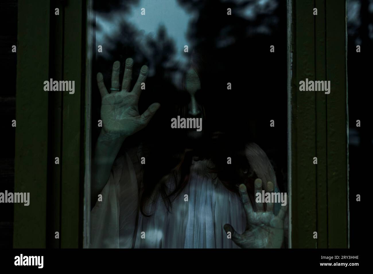 Spooky ghost looking through glass window of haunted cabin Stock Photo