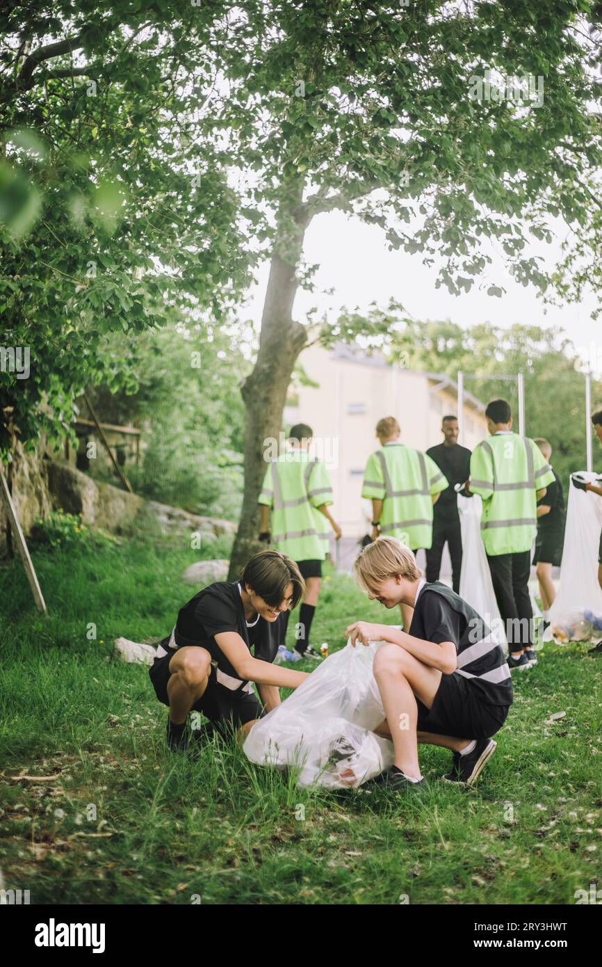 Full length of smiling teenage boys squatting while collecting garbage Stock Photo
