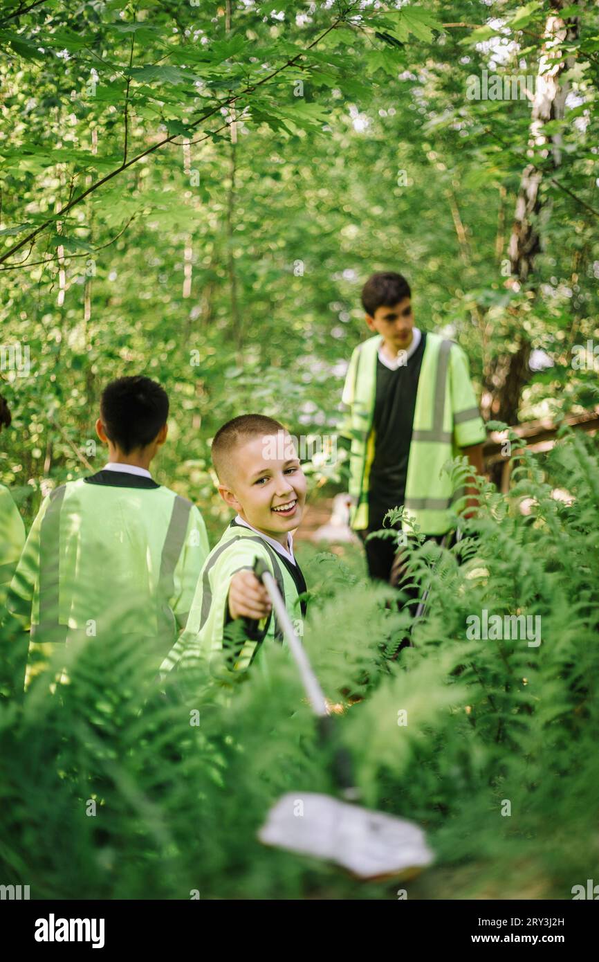 Smiling boy picking plastic garbage from green plant Stock Photo