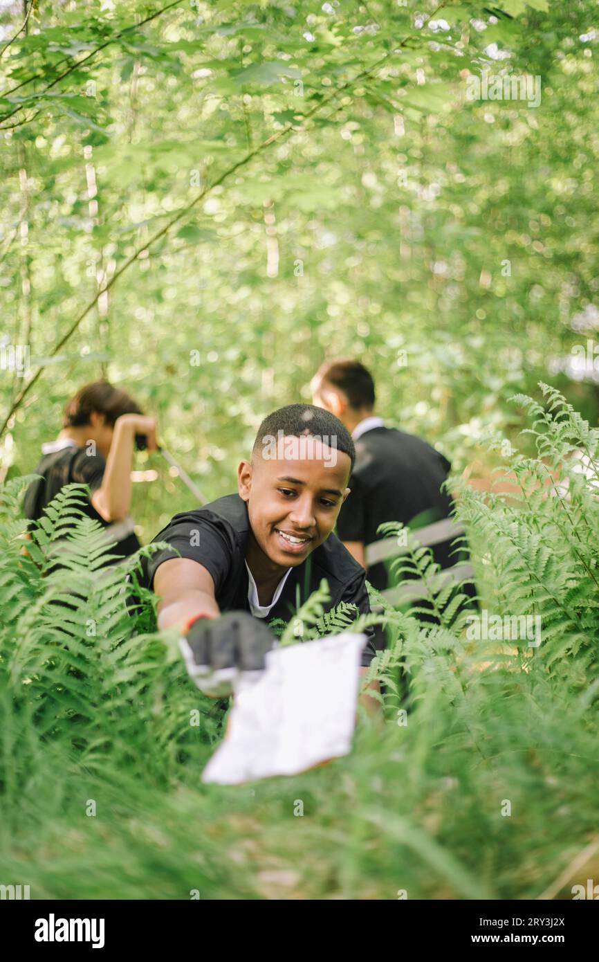 Smiling teenage boy picking up plastic from plant Stock Photo