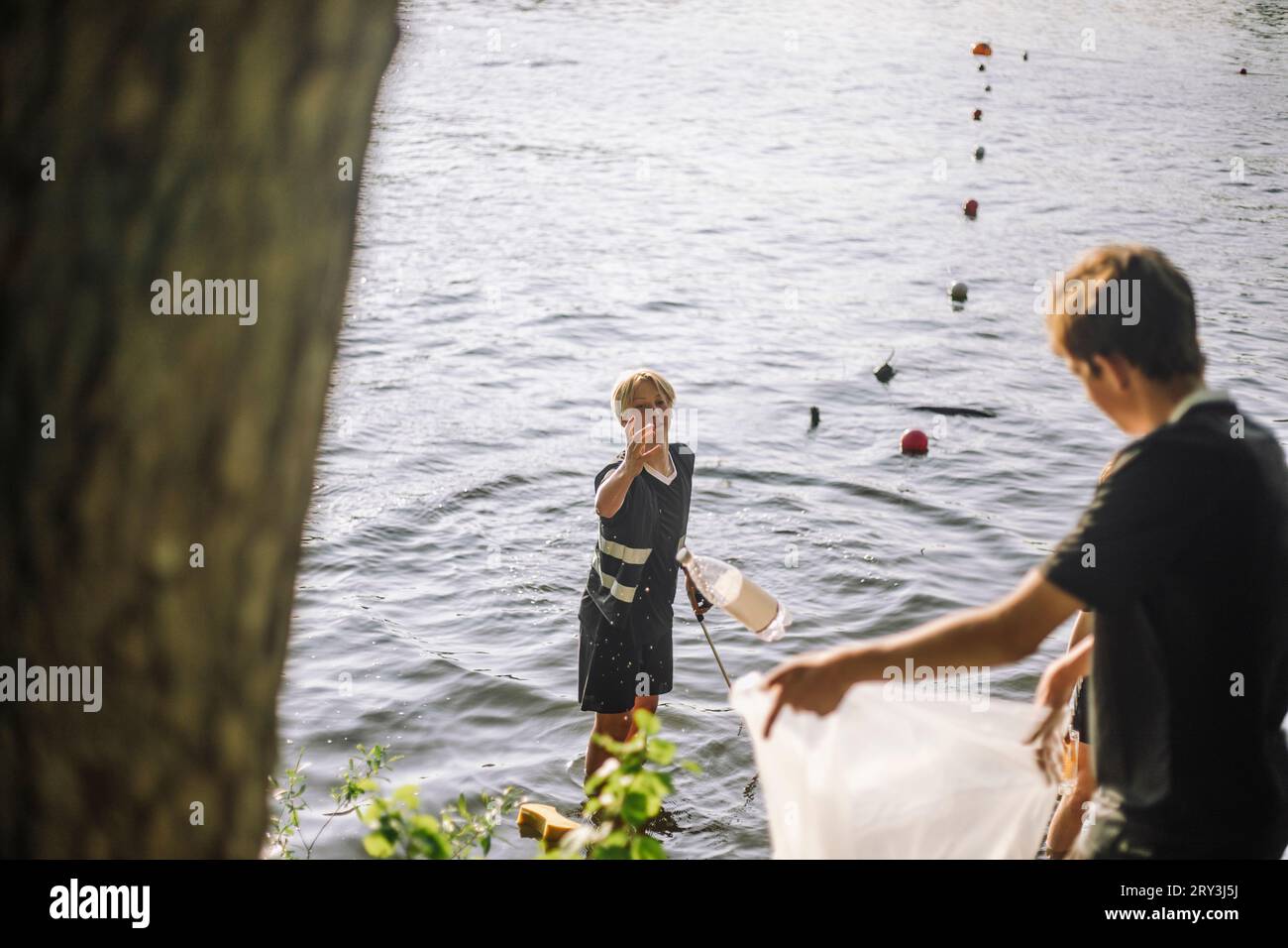 Teenage boy throwing plastic bottle in bag held by friend Stock Photo