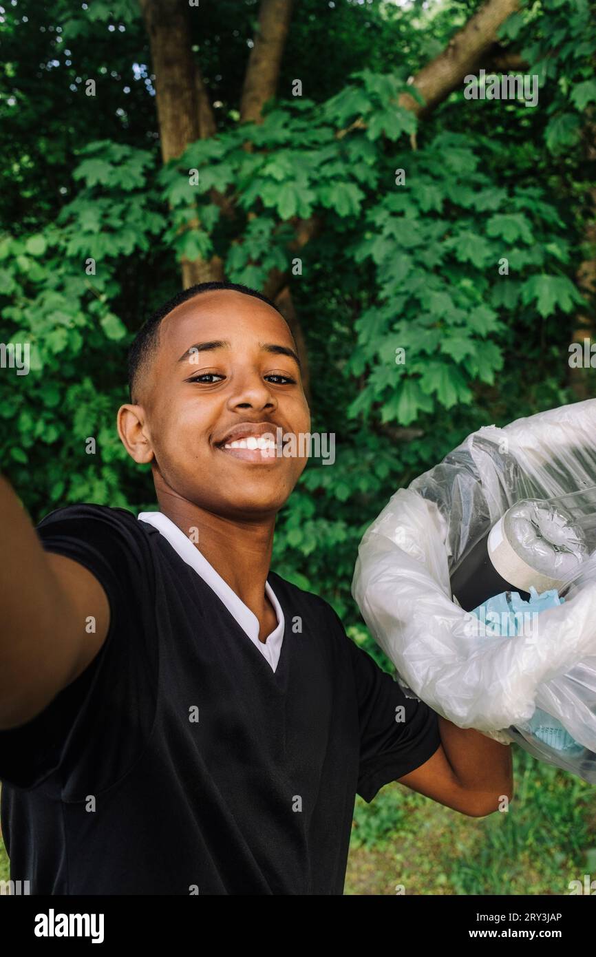 Portrait of smiling teenage boy taking selfie with garbage bag Stock Photo